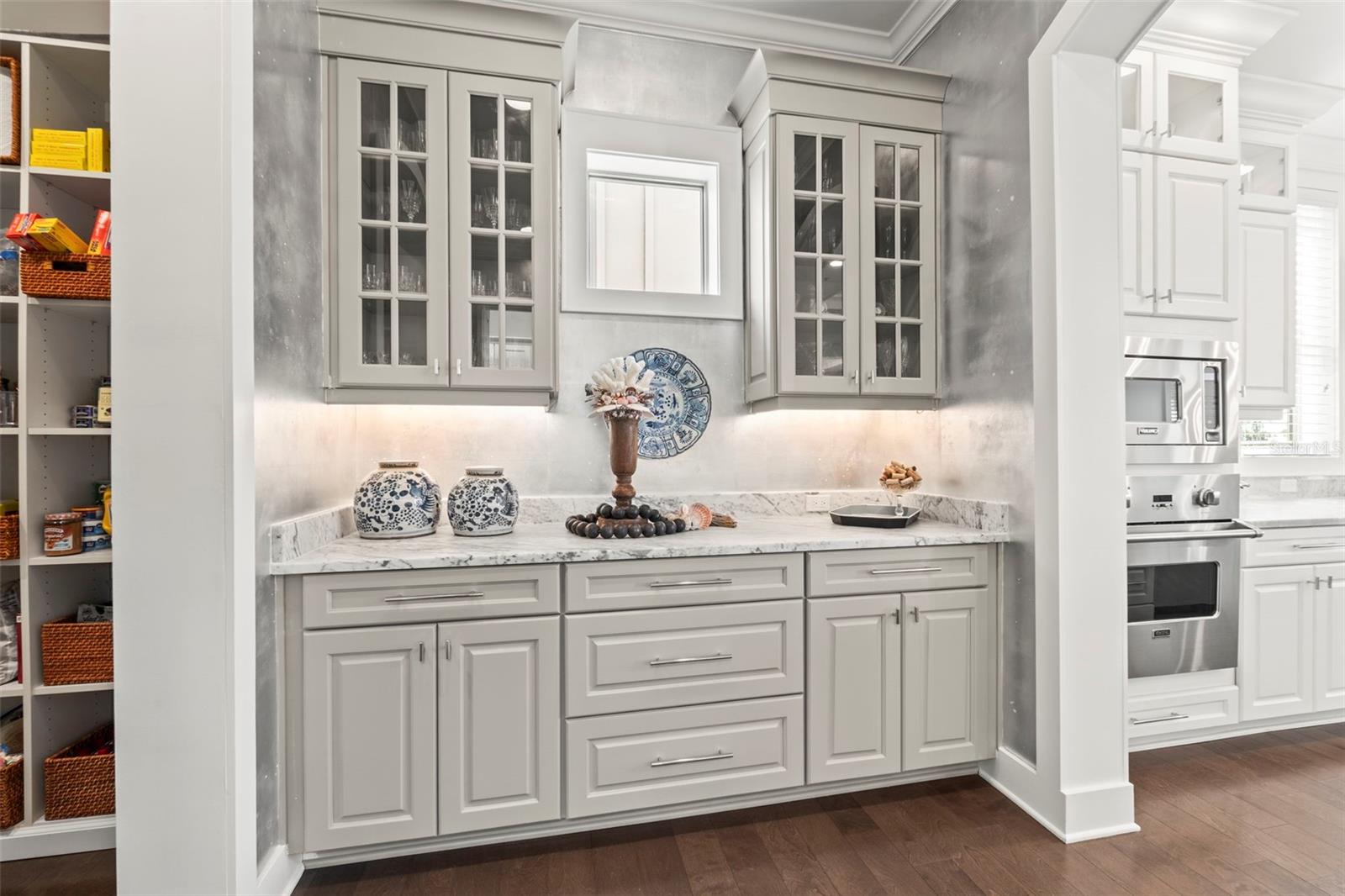 Butler's pantry with marble countertops, gorgeous designer wallpaper, custom lighting & ample storage connecting the kitchen to the large walk-in pantry and adjacent laundry room