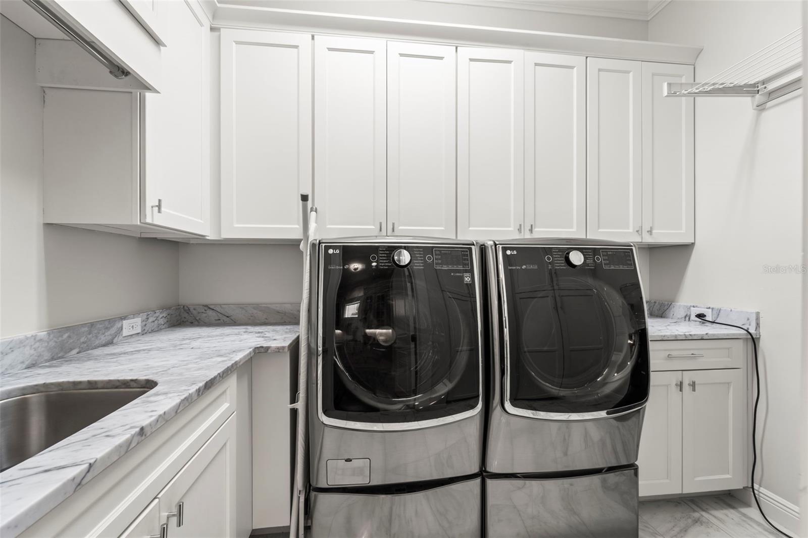 Perfectly placed laundry room with marble countertops & flooring, dual washers and extra-large capacity dryer, built-in cabinetry and full-height closets, utility sink with ample hanging & work space