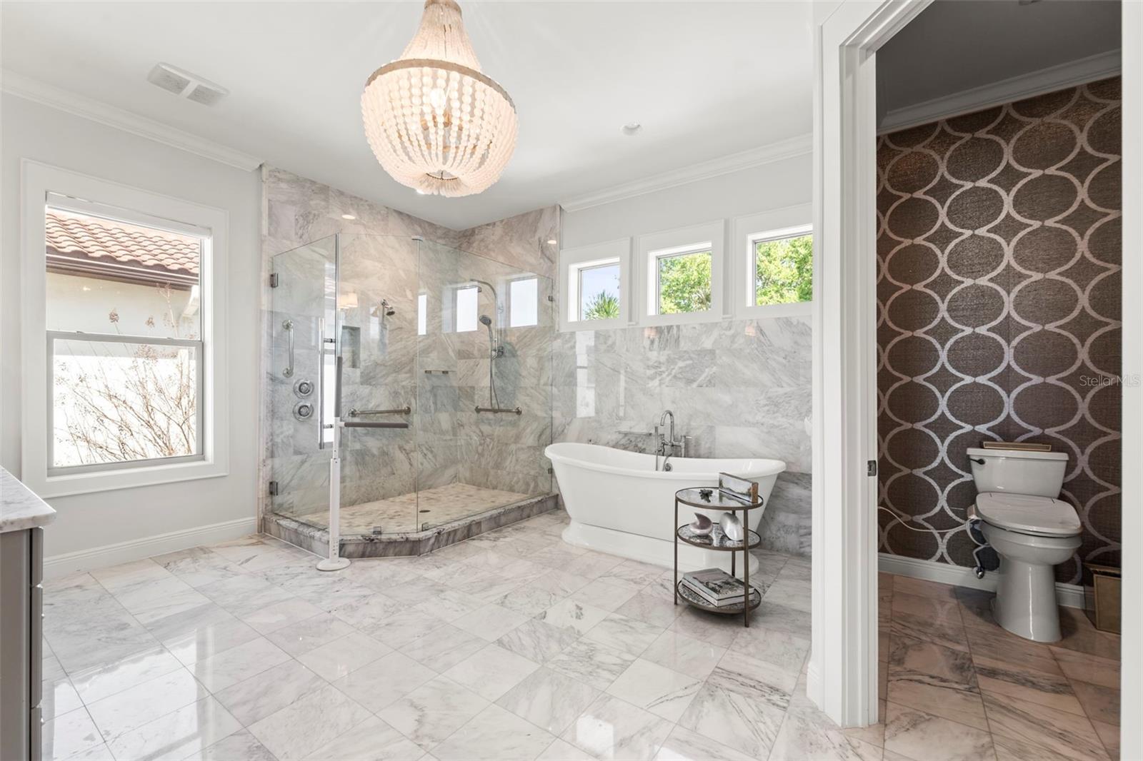 Spa-inspired, marble clad, primary bathroom featuring dual vanities, a soaking tub, a walk-in shower with dual shower heads, and bidet. This bathroom is designed for relaxation and luxury.