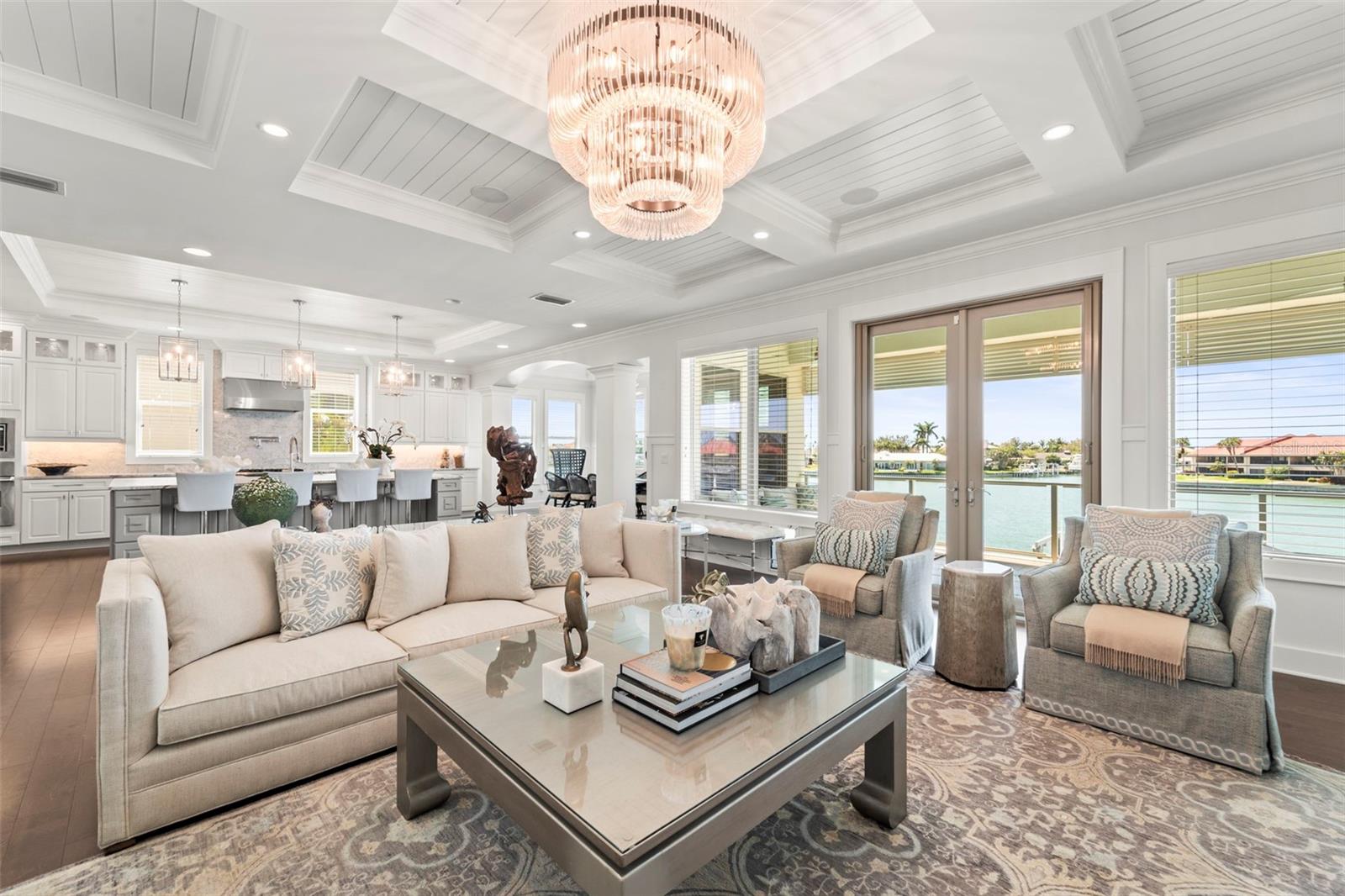 Spacious open-concept great room showcasing a custom surround sound home theatre, crystal chandelier, commissioned artwork, coffered tray ceilings, wainscoting, millwork & blinds