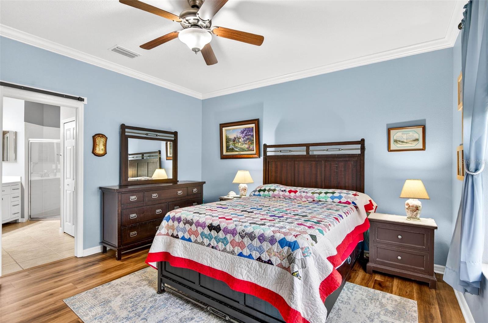 Primary bedroom with barn door entry to en suite bathroom. Luxury vinyl plank flooring, ceiling fan and crown molding.