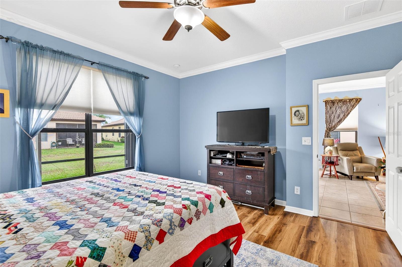 Primary bedroom with large window for natural lighting. Ceiling fan, crown molding and luxury vinyl plank flooring