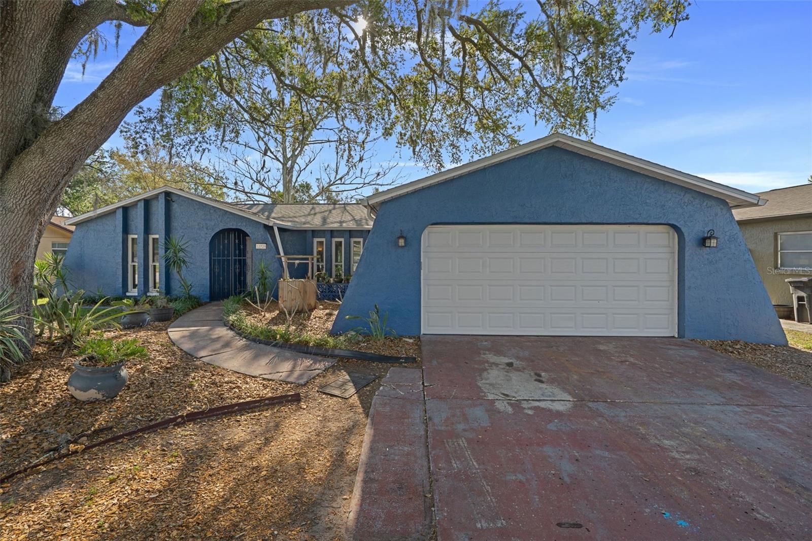 Front exterior view of the home featuring a two-car garage, mature landscaping, and shaded front yard.