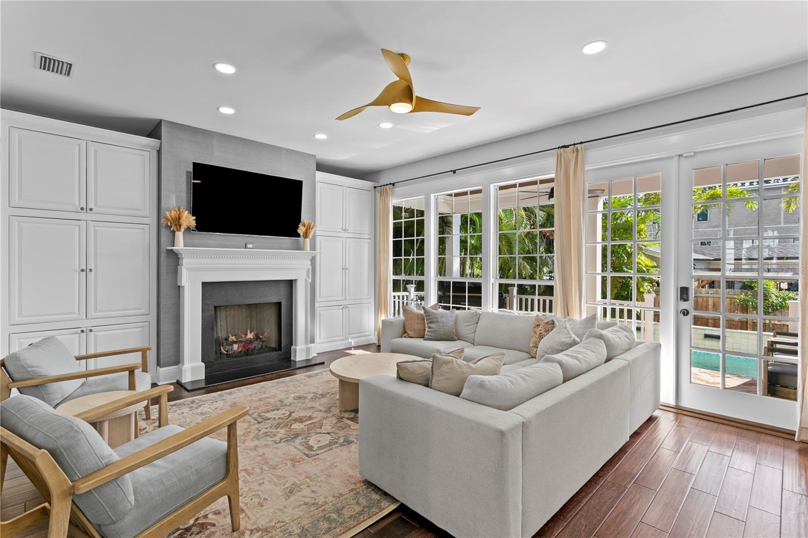 The family living room is spacious, with loads of storage for family games; cozy with the fireplace, and amazing views to the covered rear porch and pool.