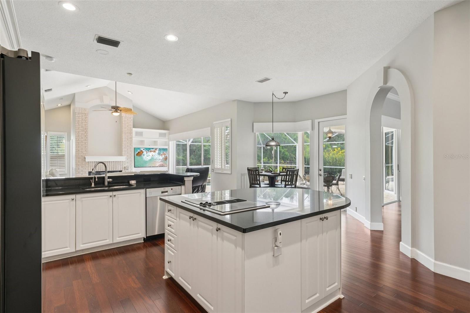 The modern kitchen is thoughtfully designed with a functional layout including an abundance of bright white cabinetry, complementary dark granite countertops a central island with extended overhang and sleek Jenn-Air downdraft cooktop. The premium appliance package also includes stainless steel built-in wall ovens and a French door refrigerator. The eat-in breakfast nook has mitered windows providing expansive views of the pool and conservation, recessed lighting, and a seamless flow into the family room.