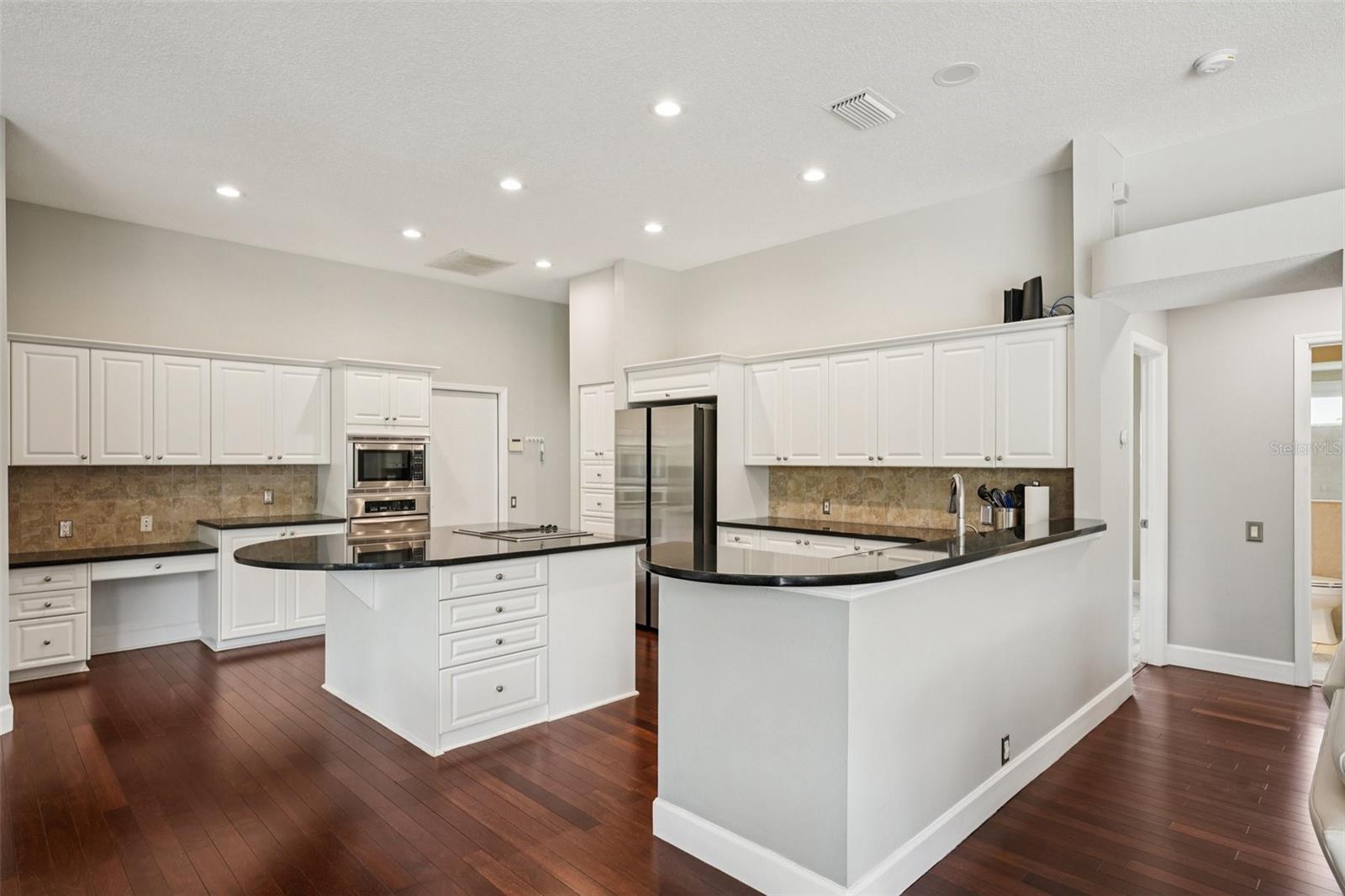 The modern kitchen is thoughtfully designed with a functional layout including an abundance of bright white cabinetry, complementary dark granite countertops a central island with extended overhang and sleek Jenn-Air downdraft cooktop. The premium appliance package also includes stainless steel built-in wall ovens and a French door refrigerator. The eat-in breakfast nook has mitered windows providing expansive views of the pool and conservation, recessed lighting, and a seamless flow into the family room.