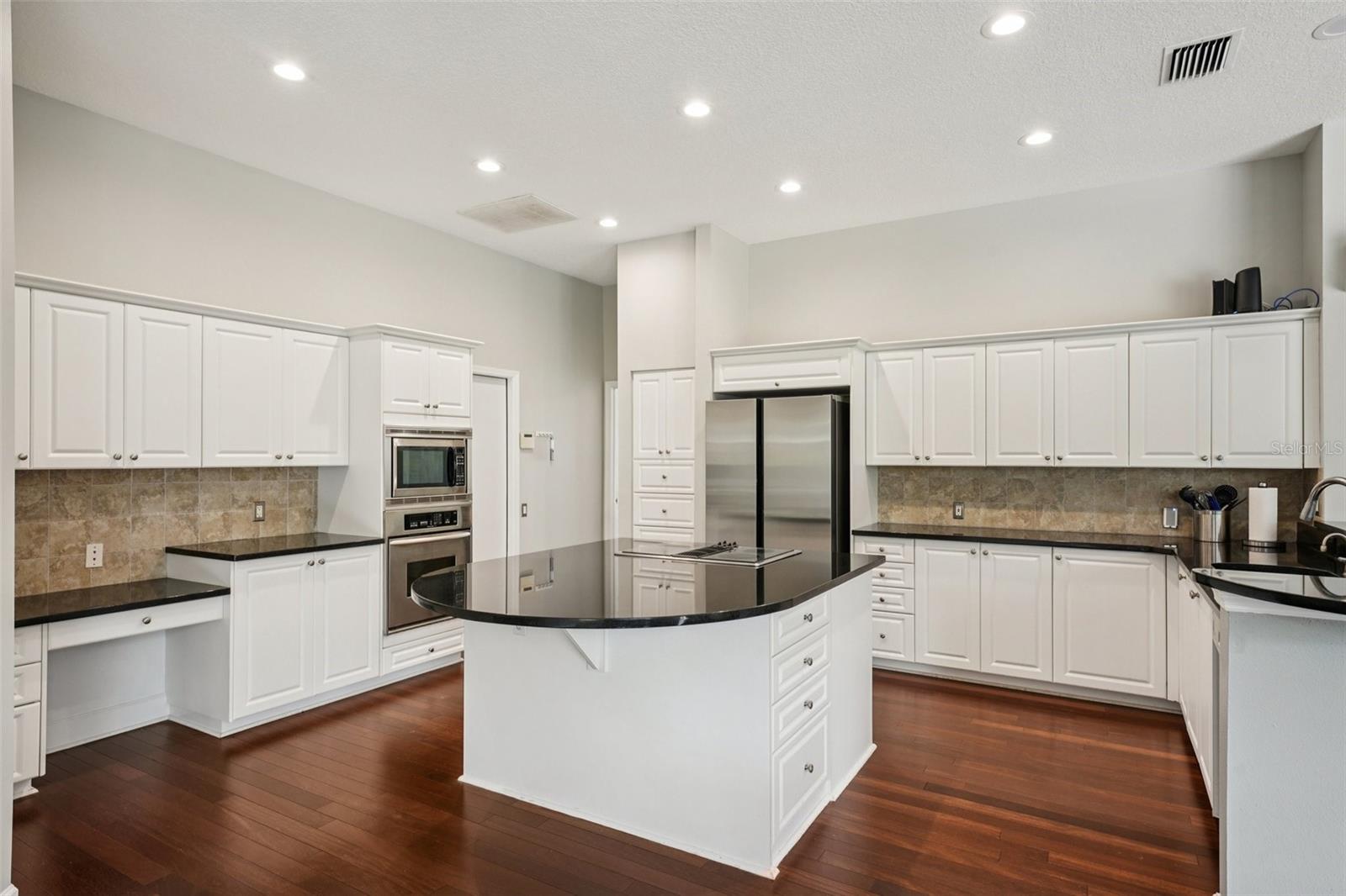 The modern kitchen is thoughtfully designed with a functional layout including an abundance of bright white cabinetry, complementary dark granite countertops a central island with extended overhang and sleek Jenn-Air downdraft cooktop. The premium appliance package also includes stainless steel built-in wall ovens and a French door refrigerator. The eat-in breakfast nook has mitered windows providing expansive views of the pool and conservation, recessed lighting, and a seamless flow into the family room.