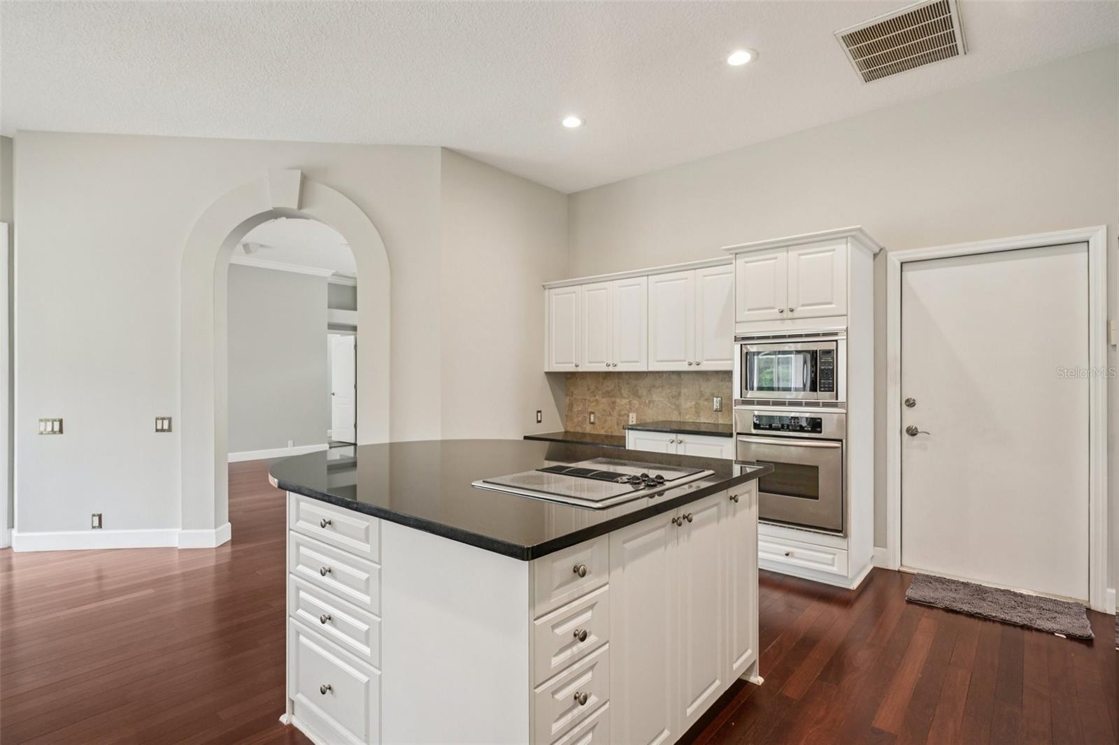 The modern kitchen is thoughtfully designed with a functional layout including an abundance of bright white cabinetry, complementary dark granite countertops a central island with extended overhang and sleek Jenn-Air downdraft cooktop. The premium appliance package also includes stainless steel built-in wall ovens and a French door refrigerator. The eat-in breakfast nook has mitered windows providing expansive views of the pool and conservation, recessed lighting, and a seamless flow into the family room.