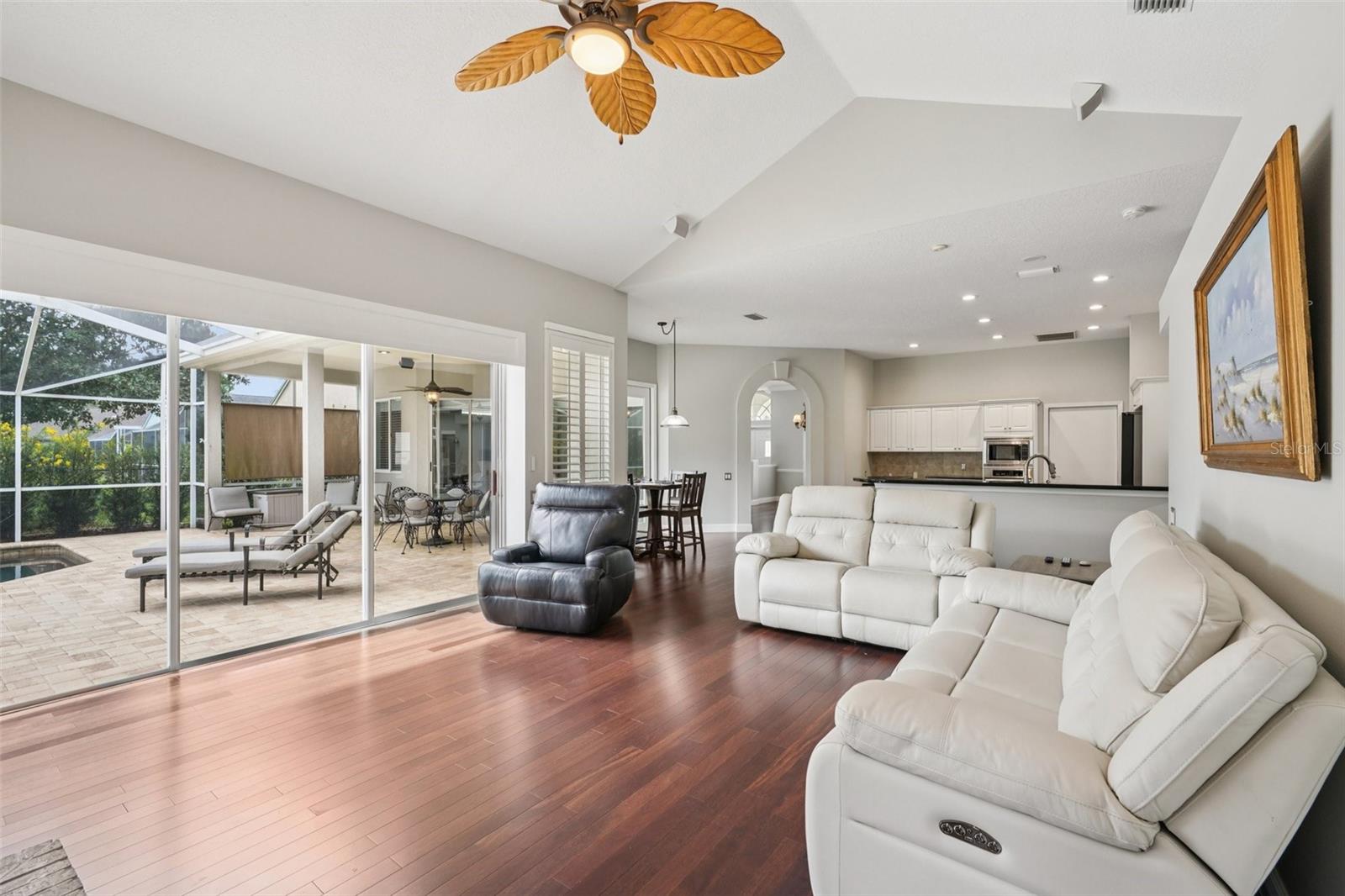 The family room is an ideal gathering space with vaulted ceilings, expansive triple glass sliders opening to the pool area, built-in shelving with media space, and a striking wood-burning fireplace.