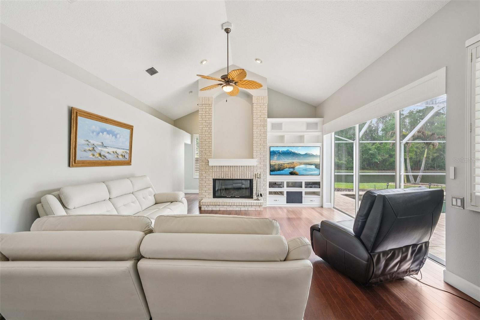 The family room is an ideal gathering space with vaulted ceilings, expansive triple glass sliders opening to the pool area, built-in shelving with media space, and a striking wood-burning fireplace.