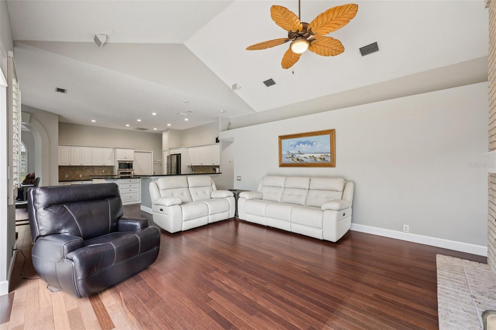 The family room is an ideal gathering space with vaulted ceilings, expansive triple glass sliders opening to the pool area, built-in shelving with media space, and a striking wood-burning fireplace.