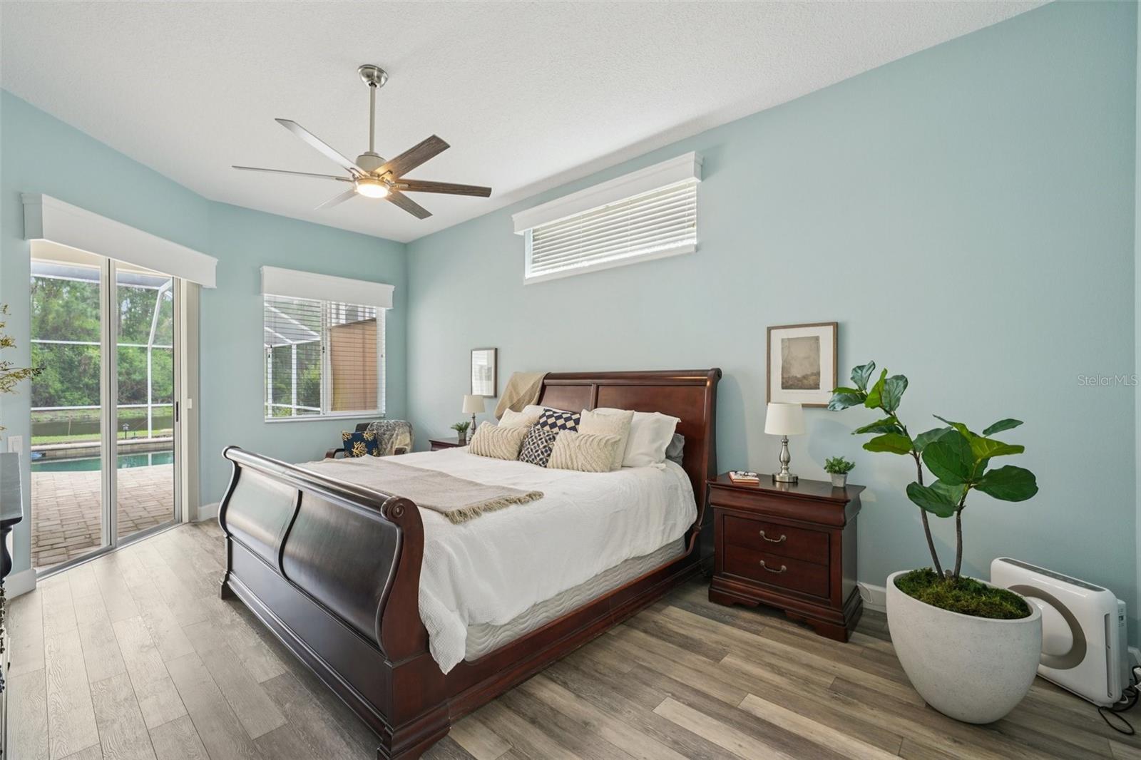 . The spacious primary bedroom suite features luxury vinyl flooring, abundant natural light, and sliding glass doors that frame peaceful morning views and provide private access to the pool.