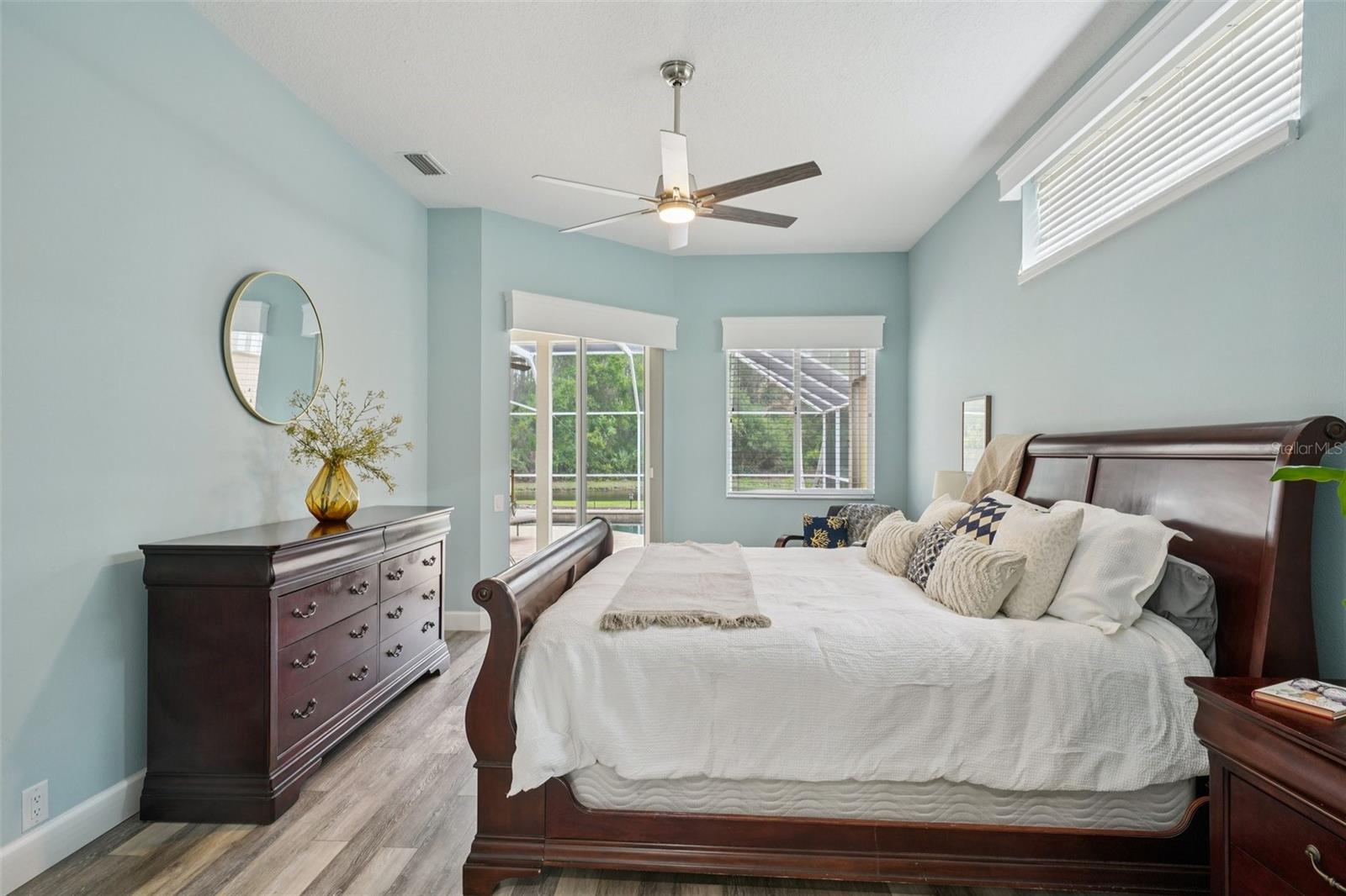 . The spacious primary bedroom suite features luxury vinyl flooring, abundant natural light, and sliding glass doors that frame peaceful morning views and provide private access to the pool.