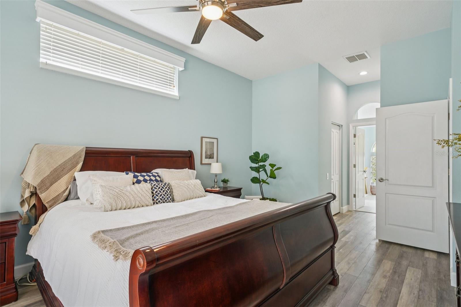 . The spacious primary bedroom suite features luxury vinyl flooring, abundant natural light, and sliding glass doors that frame peaceful morning views and provide private access to the pool.