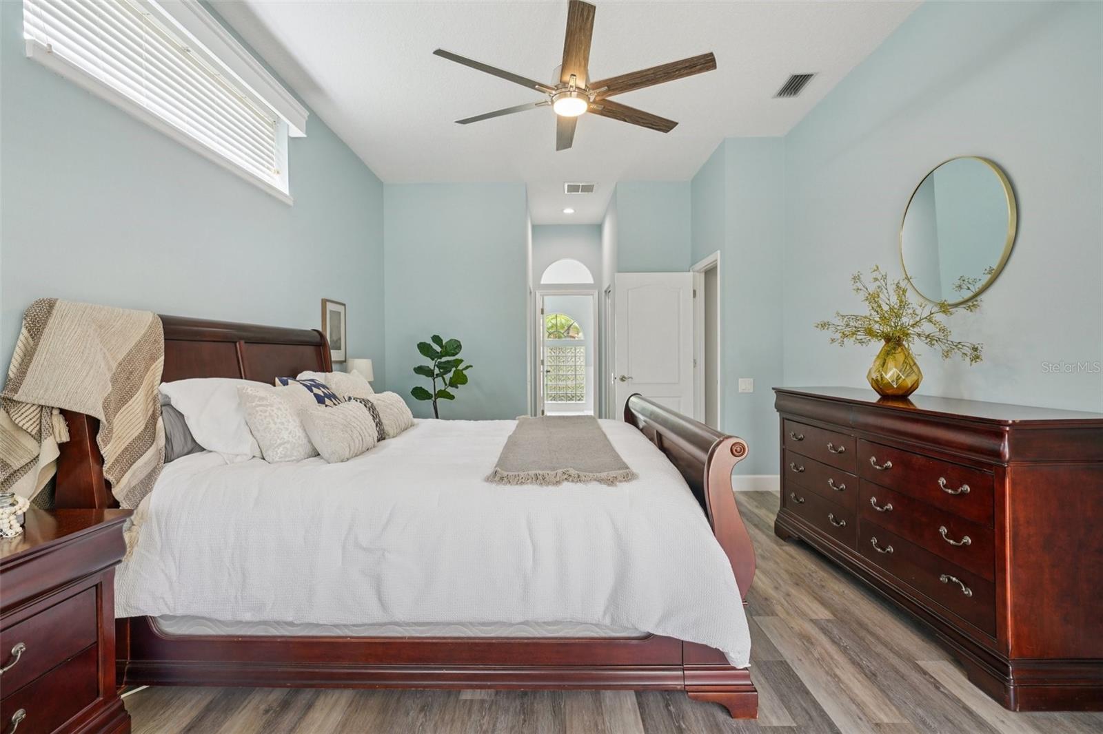 . The spacious primary bedroom suite features luxury vinyl flooring, abundant natural light, and sliding glass doors that frame peaceful morning views and provide private access to the pool.