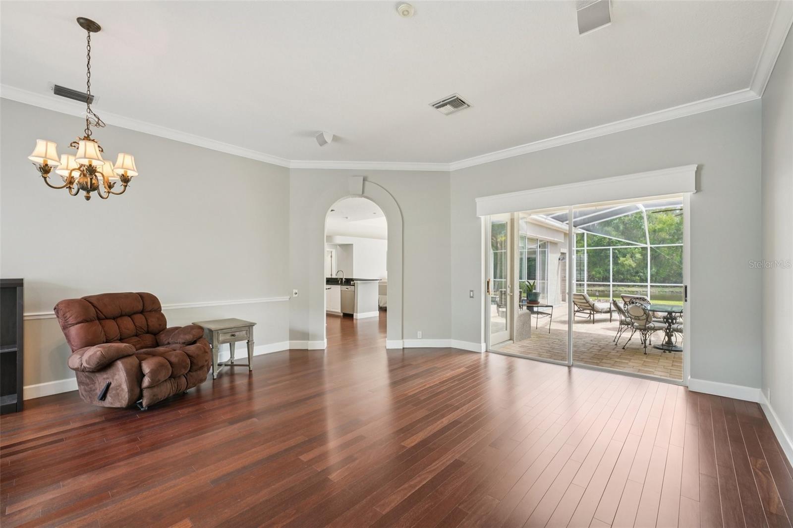 Living room features gorgeous cherry engineered hardwood floors, glass sliders connecting out to the pool area, ceiling home audio speakers, and architectural features connecting throughout the home.
