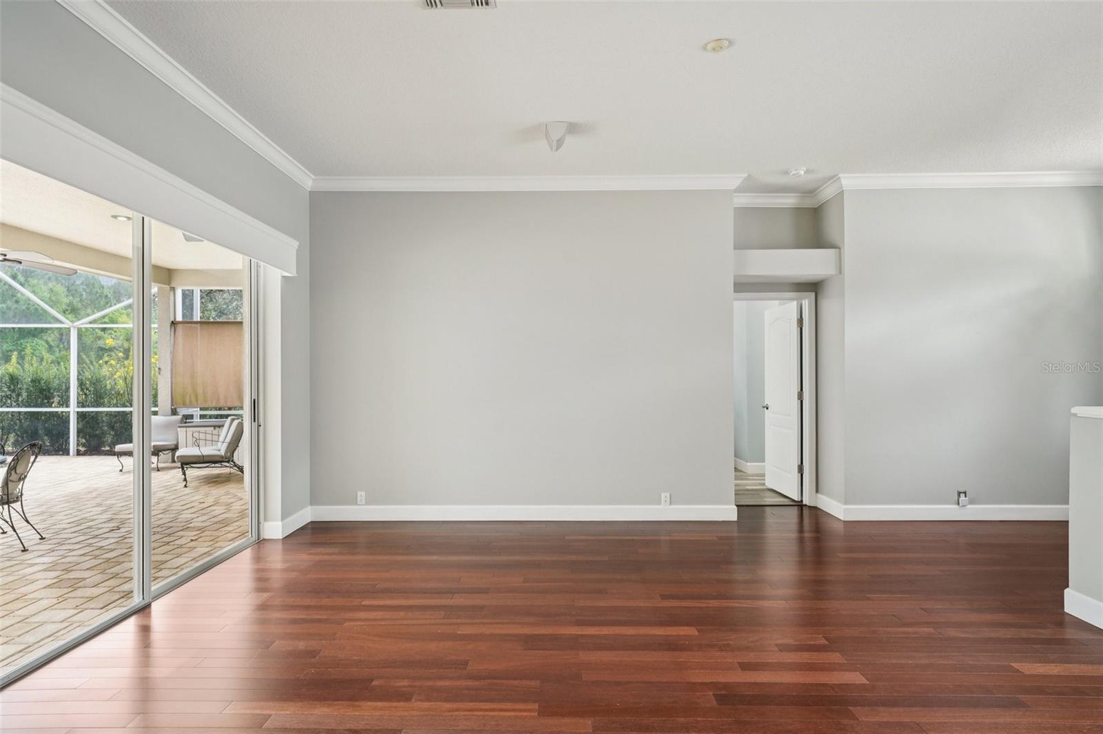 Living room features gorgeous cherry engineered hardwood floors, glass sliders connecting out to the pool area, ceiling home audio speakers, and architectural features connecting throughout the home.