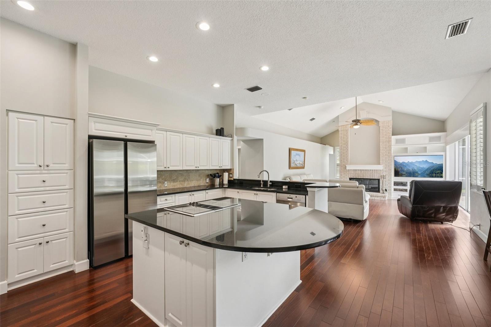 The modern kitchen is thoughtfully designed with a functional layout including an abundance of bright white cabinetry, complementary dark granite countertops a central island with extended overhang and sleek Jenn-Air downdraft cooktop. The premium appliance package also includes stainless steel built-in wall ovens and a French door refrigerator. The eat-in breakfast nook has mitered windows providing expansive views of the pool and conservation, recessed lighting, and a seamless flow into the family room.