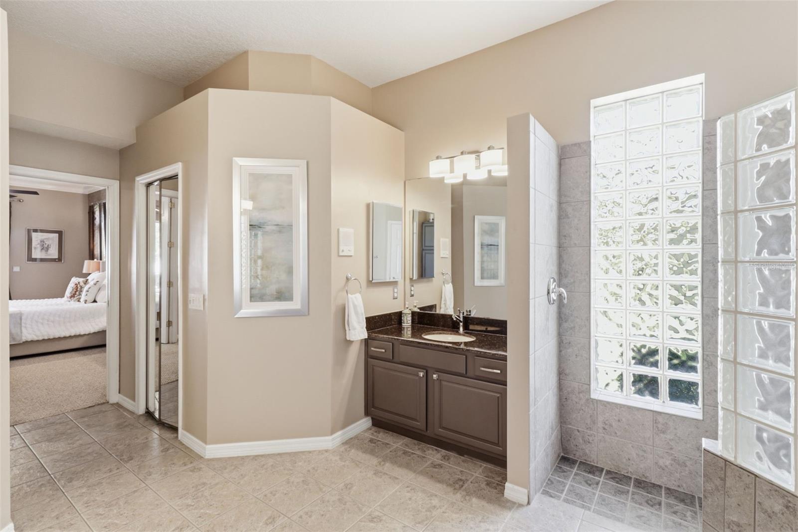Primary en-suite featuring a spacious vanity, walk-in shower with glass block detail, and open, functional layout