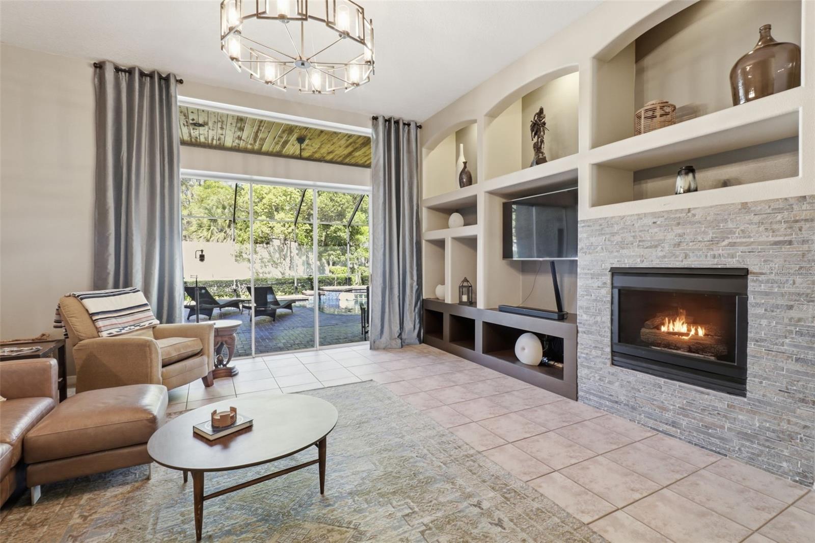 Light-filled living room featuring a fireplace, custom built-ins, and sliding glass doors with views of the pool