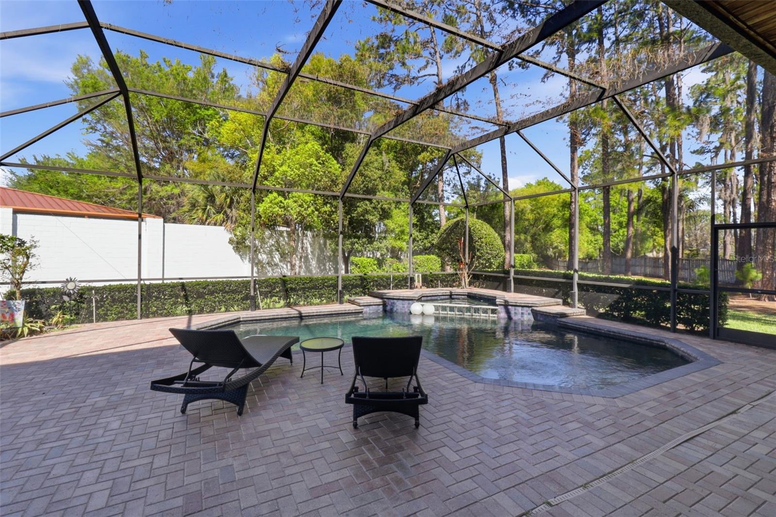 Spacious screened pool and spa with waterfall feature, surrounded by paver patio and private, tree-lined backyard