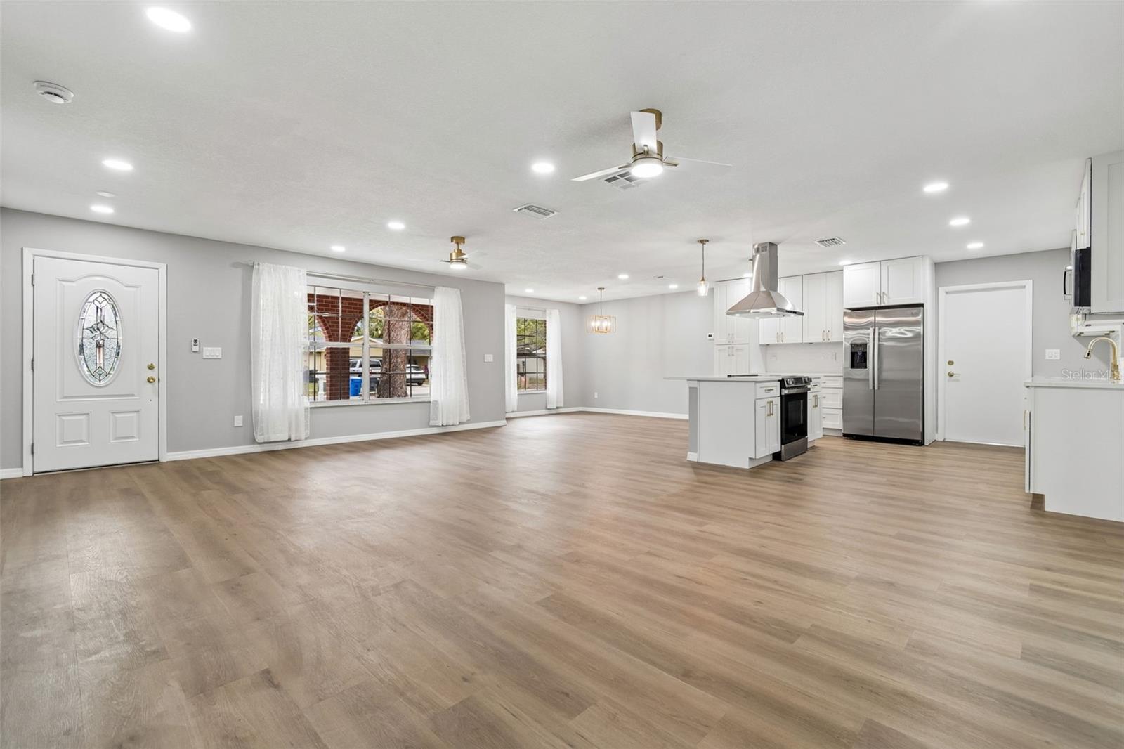 Spacious living room with wood-look flooring, recessed lighting, and a large front window providing natural light.