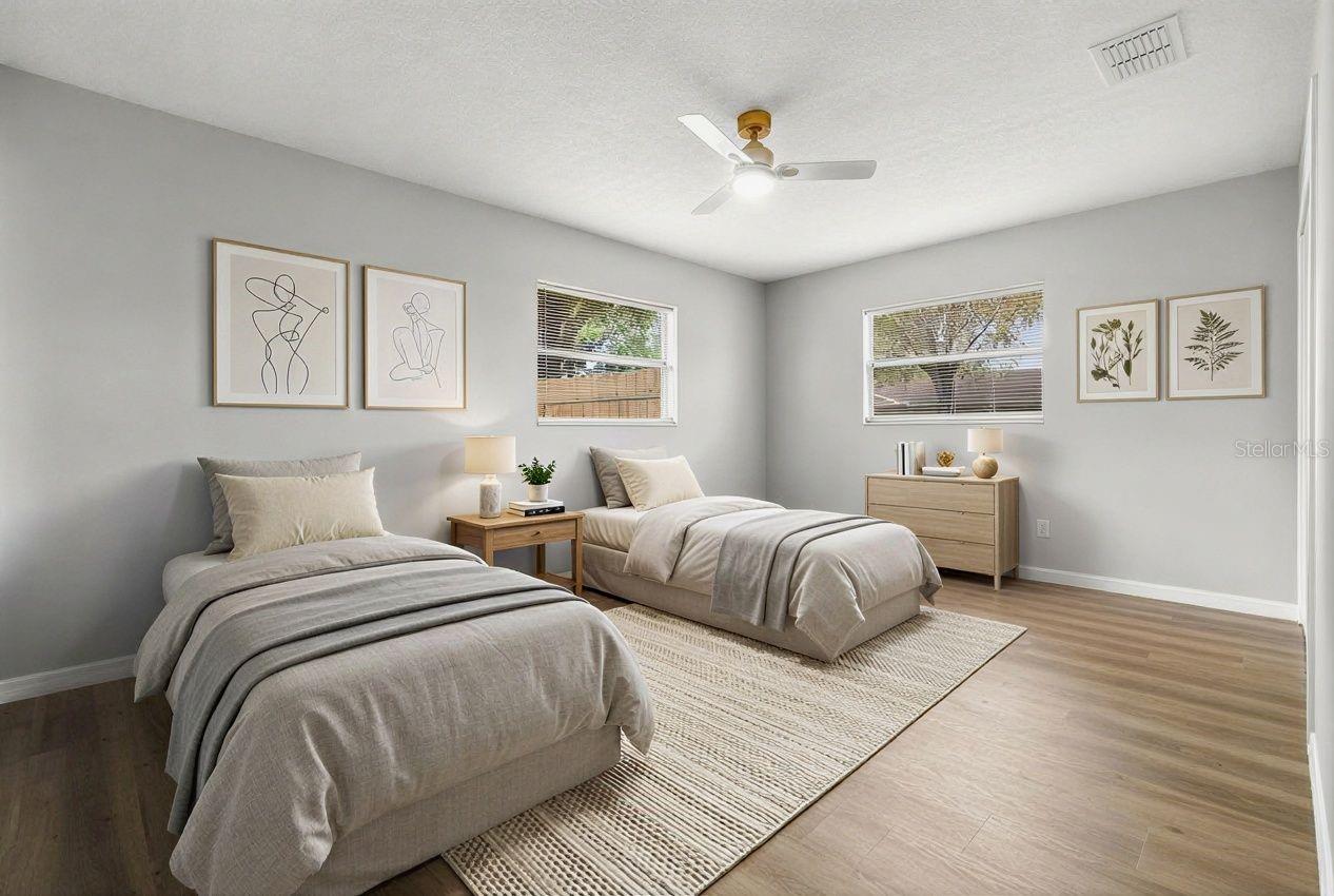 Spacious bedroom with wood-look flooring, ceiling fan, and natural light from two windows, offering flexible layout options.