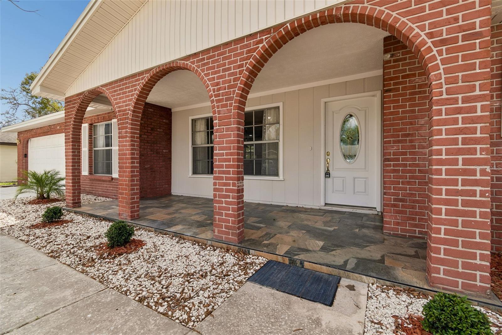 Covered front porch with distinctive brick arches and tiled flooring, offering a shaded seating area and welcoming entry.