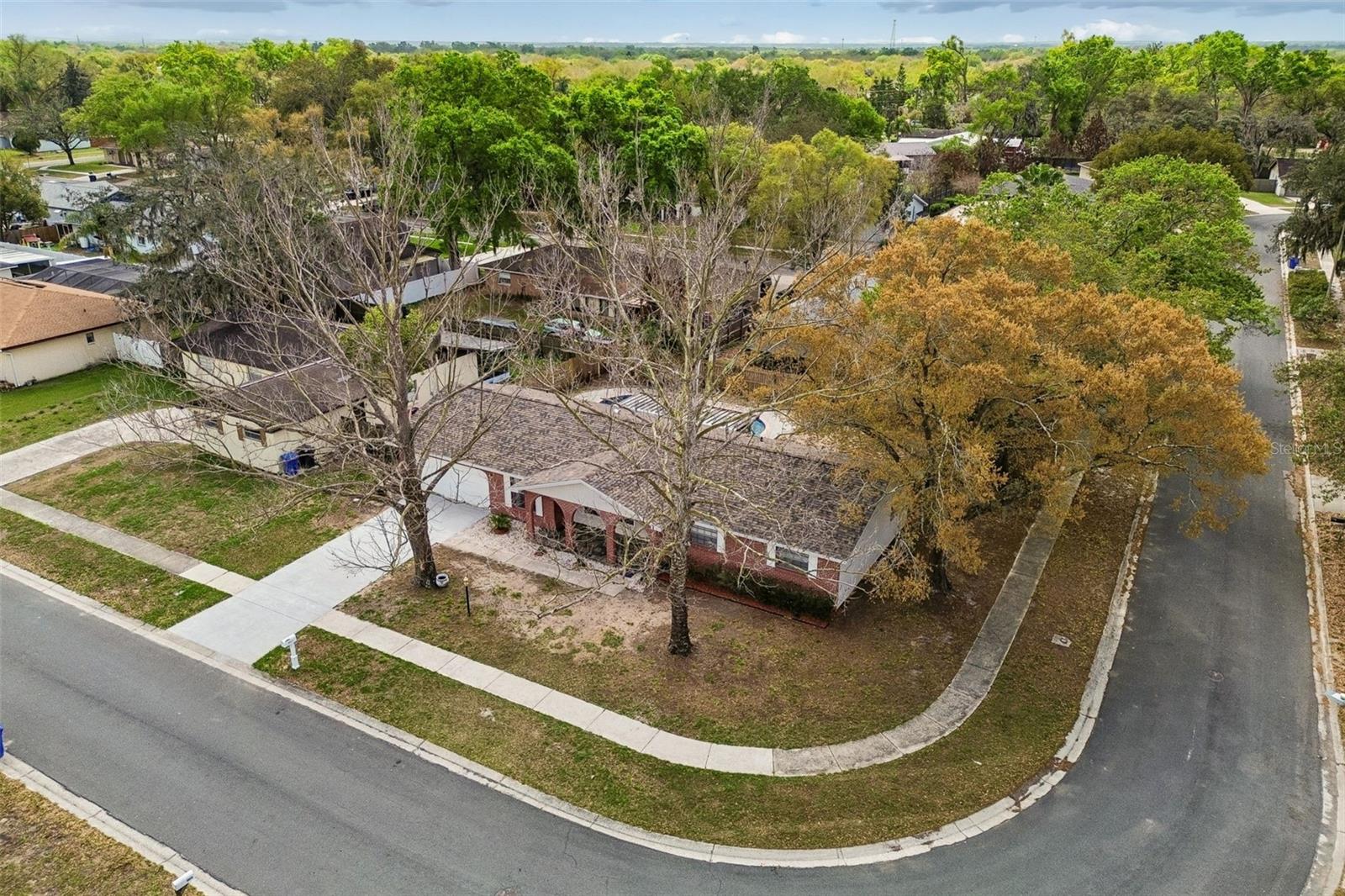 Corner lot aerial view showing the home’s position in the neighborhood, mature trees, and surrounding residential streets.