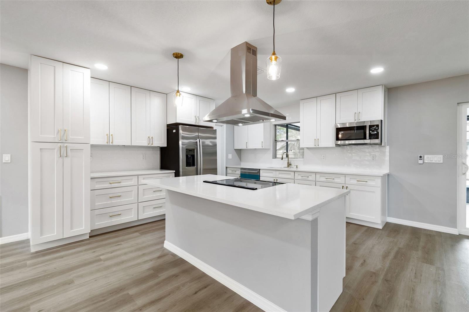 Fully renovated kitchen featuring white cabinetry, large center island, quartz countertops, stainless steel appliances, and modern lighting.