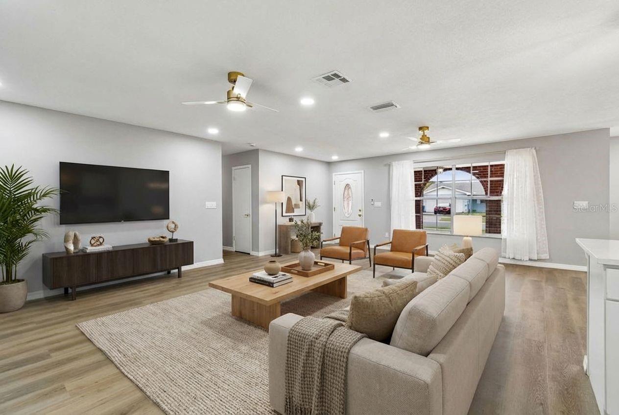 Spacious living room with wood-look flooring, recessed lighting, and a large front window providing natural light.
