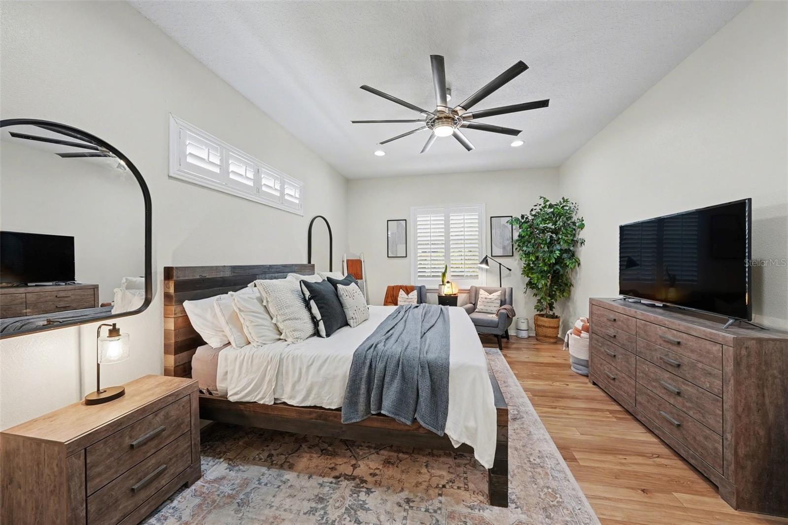 An oversized room with ceiling fan, natural light filtered with plantation shutters, and two walk in closets.