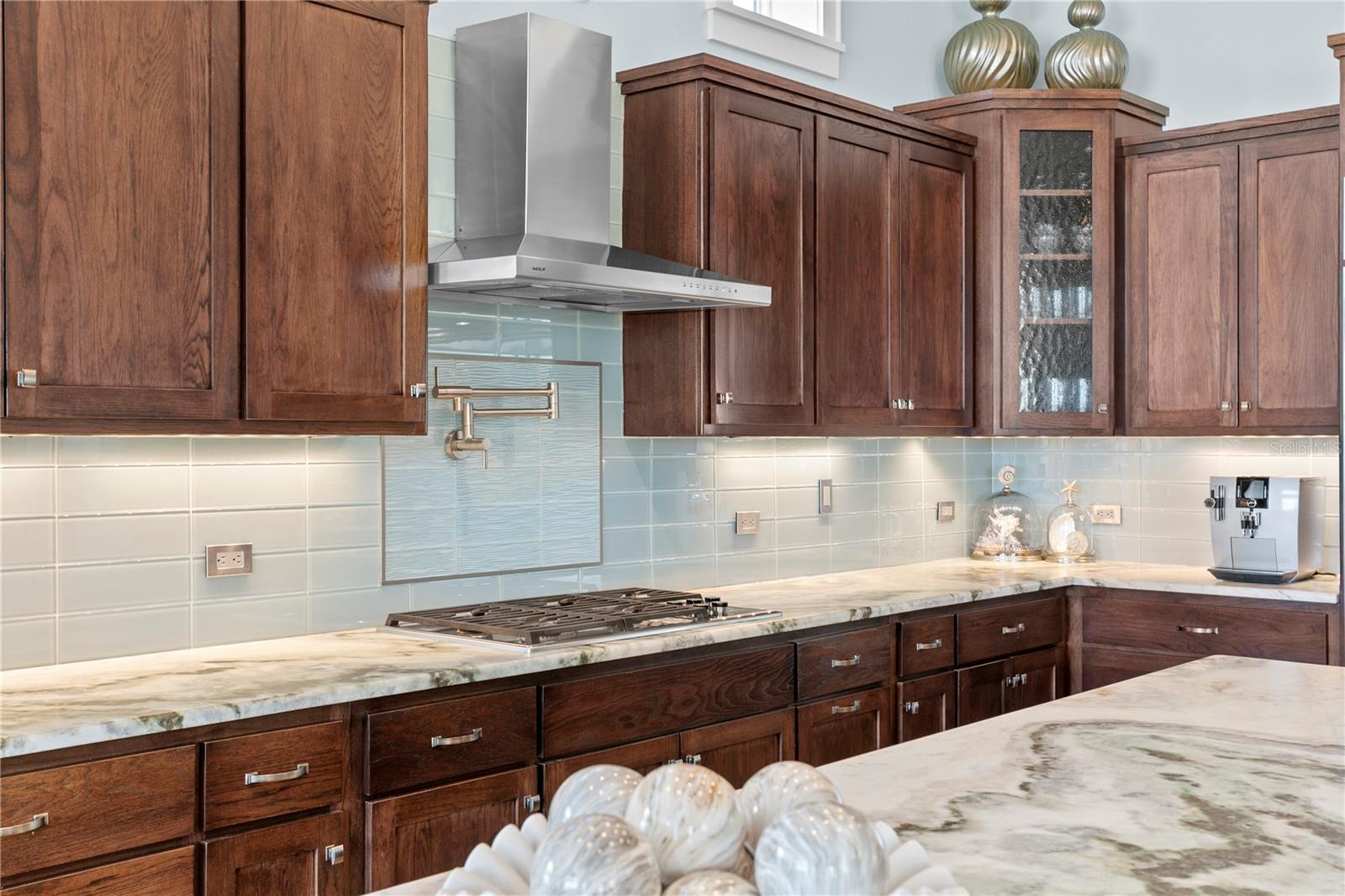Detail view of glass backsplash; pot filler, Wolf gas cooktop; notice the details in the stone counters.