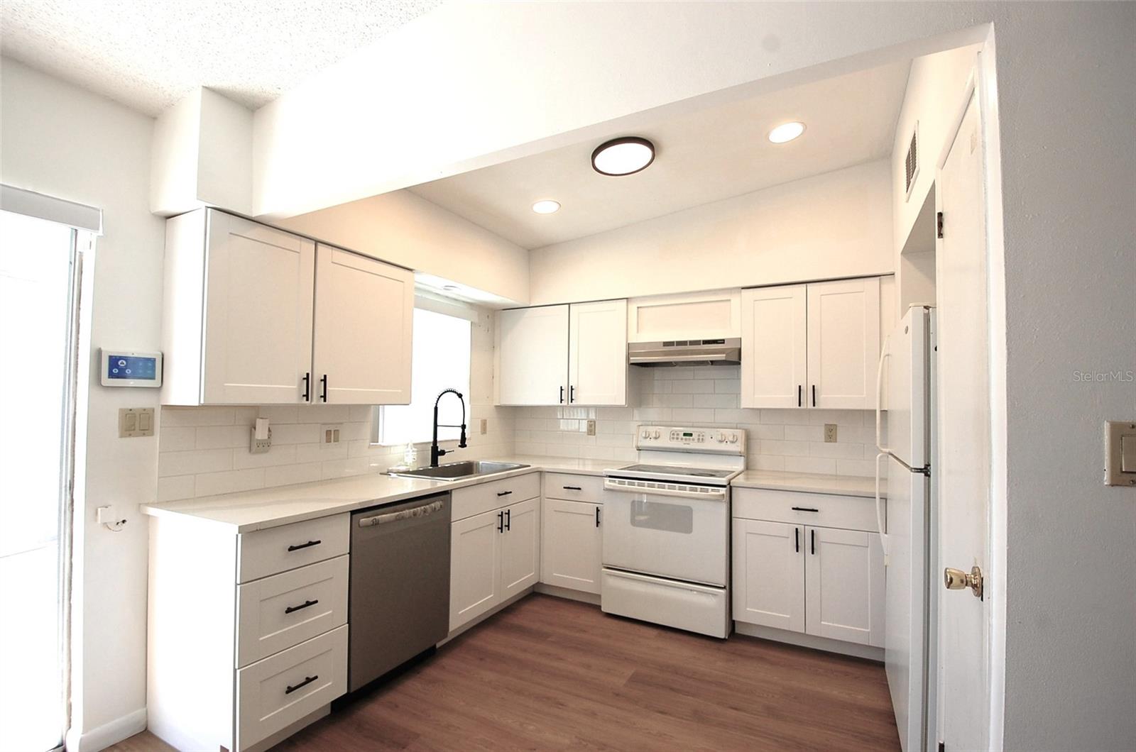 Updated bright and light kitchen with white shaker-style cabinetry, subway tile backsplash, recessed lighting, new dish washer, window overlooking the pool and open to the dining room and living room.