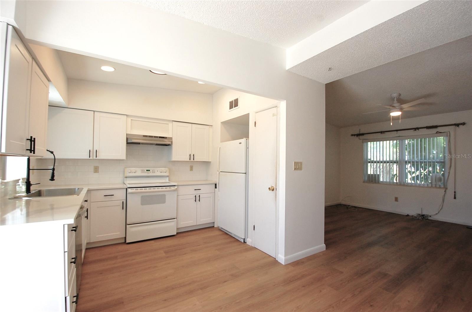 Updated bright and light kitchen with white shaker-style cabinetry, subway tile backsplash, recessed lighting, new dish washer, window overlooking the pool and open to the dining room and living room.
