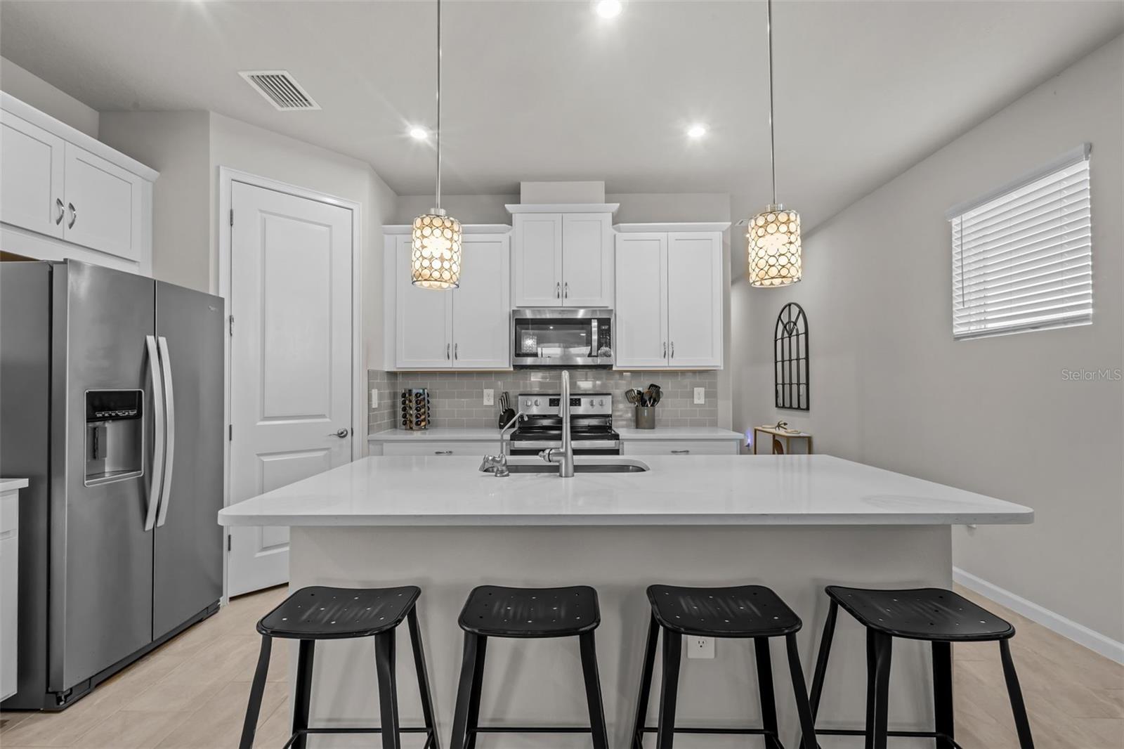 Upgraded kitchen featuring quartz countertops, white cabinetry, stainless steel appliances, and designer pendant lighting.