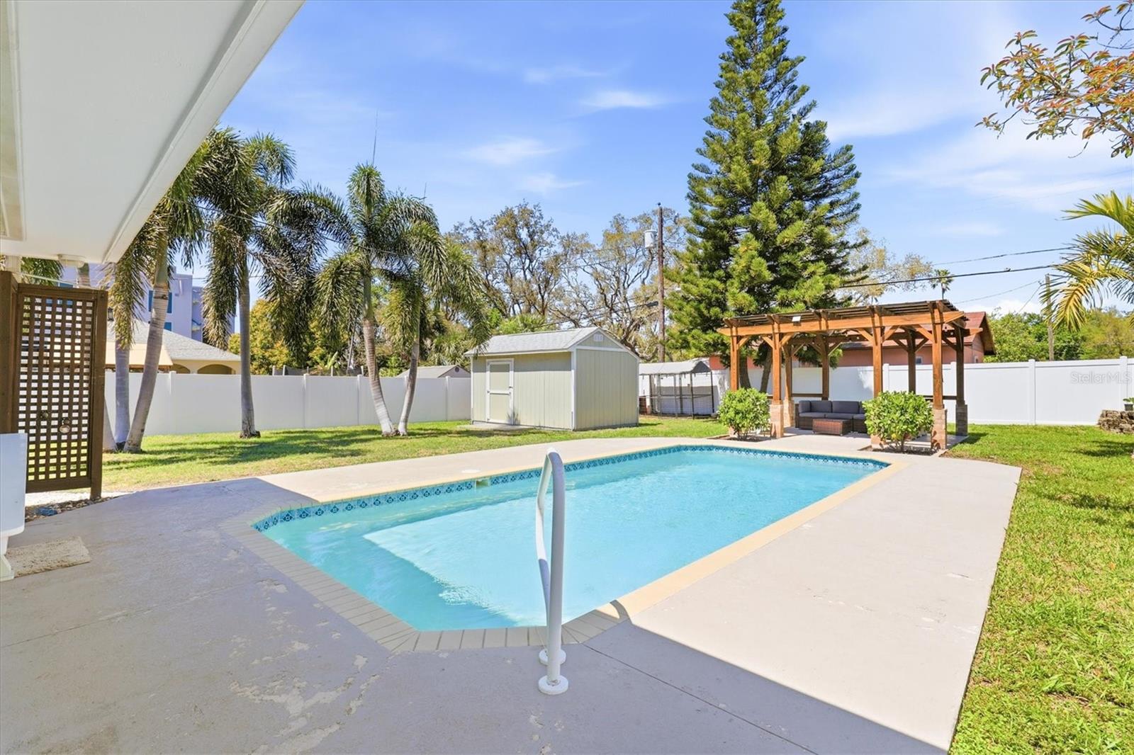 Private backyard oasis featuring a sparkling pool, ample lounging space, and a generous-sized storage shed