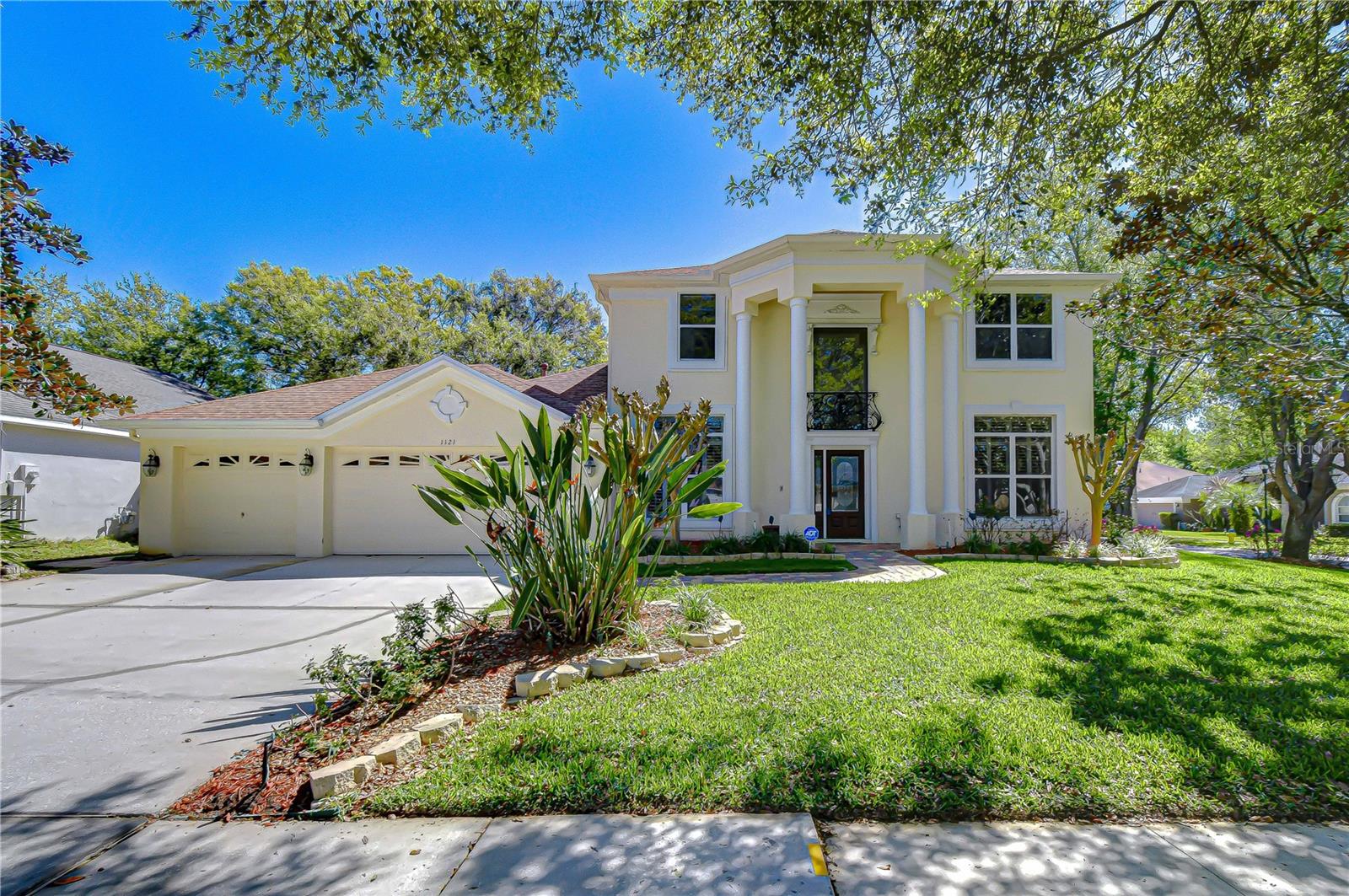 Striking two-story facade with grand columns, double garage, and lush landscaping on a wide driveway.