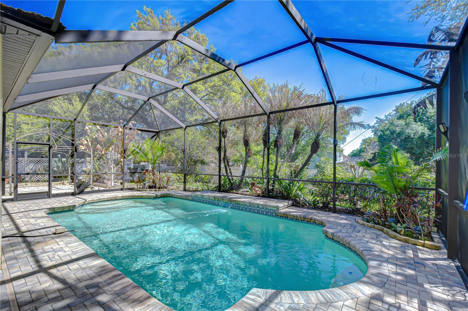 Screen-enclosed pool with paver deck and lush landscaping creates a private Florida backyard retreat.