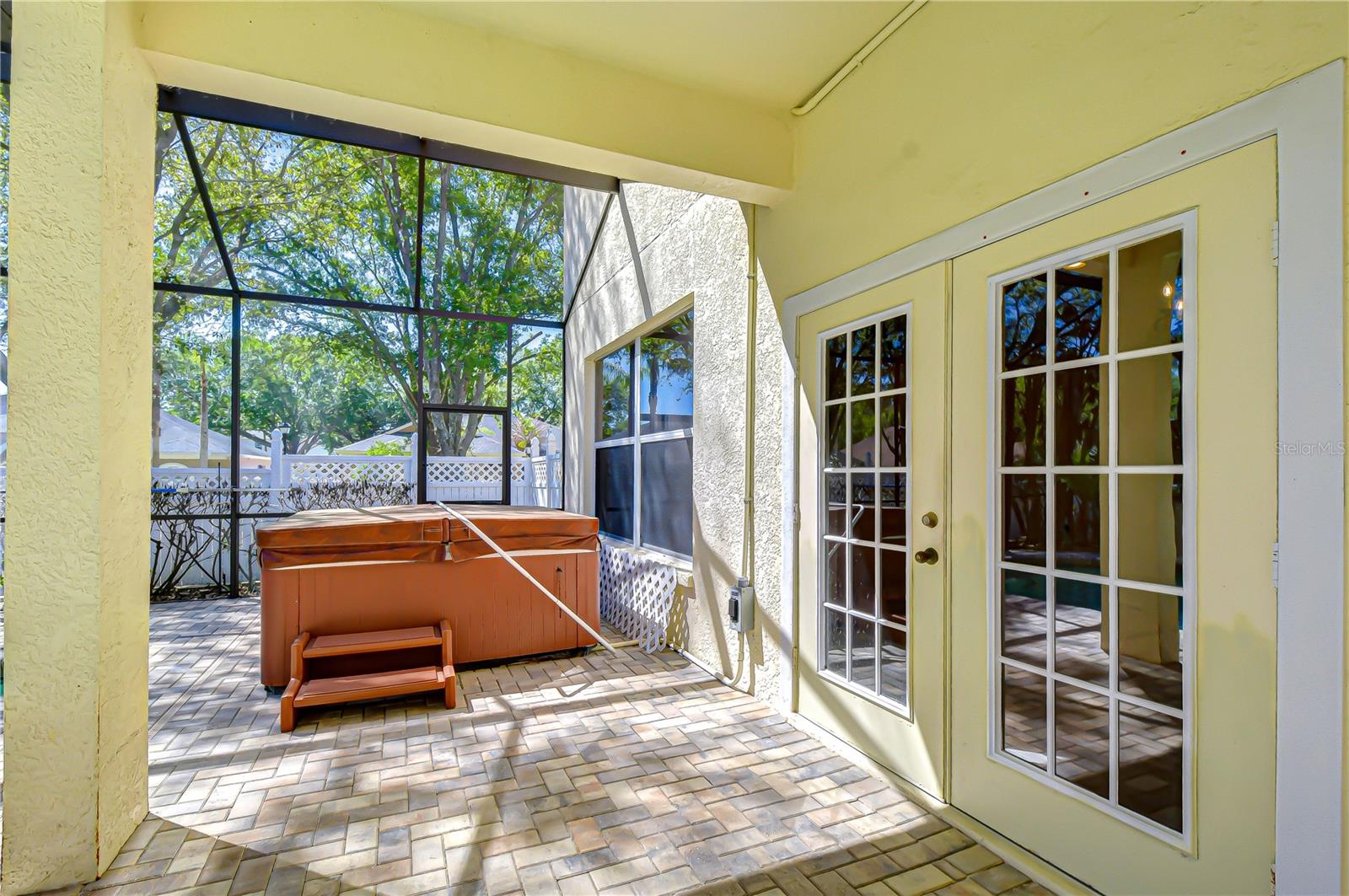 Screened lanai with paver patio and French doors, offering breezy indoor-outdoor flow and shade.