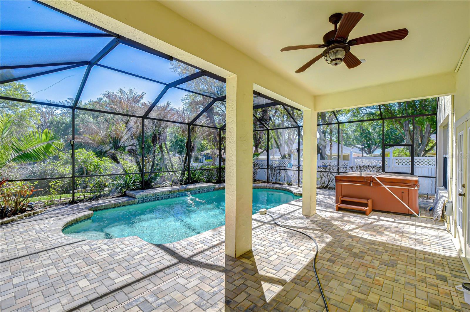 Screened lanai with sparkling pool, expansive paver patio, and ceiling fan for breezy outdoor living.
