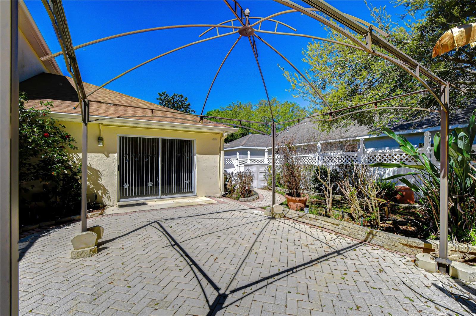 Spacious paver patio with pergola, garden beds, and fenced backyard for outdoor living.