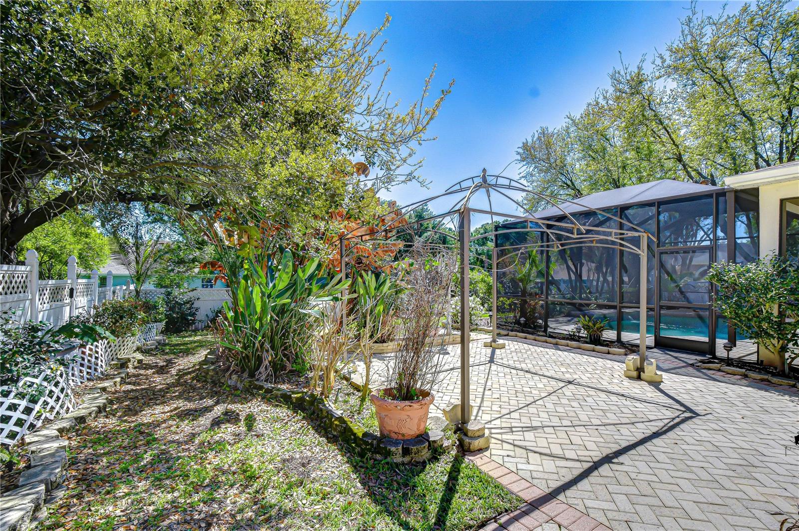 Sunlit paver patio with lush landscaping, privacy fencing, and a screened pool enclosure for outdoor living.