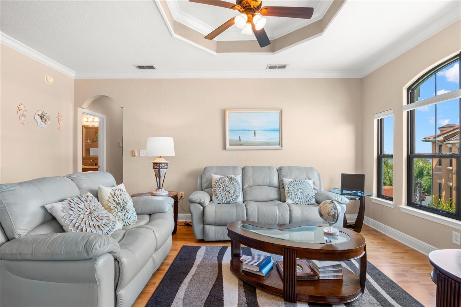 Natural light filters through arched windows, highlighting the tray ceiling detail and creating a bright, inviting space.