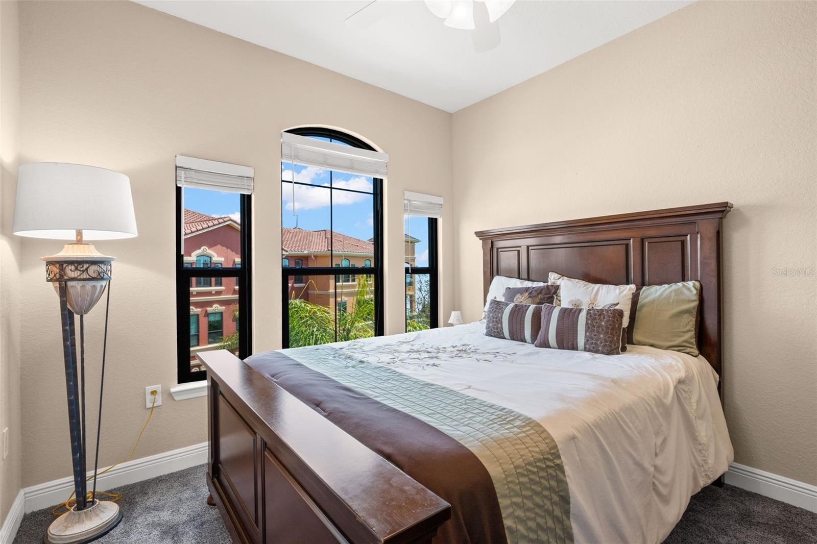 The second bedroom features plush carpet underfoot, a ceiling fan, and arched windows that bring in natural light.