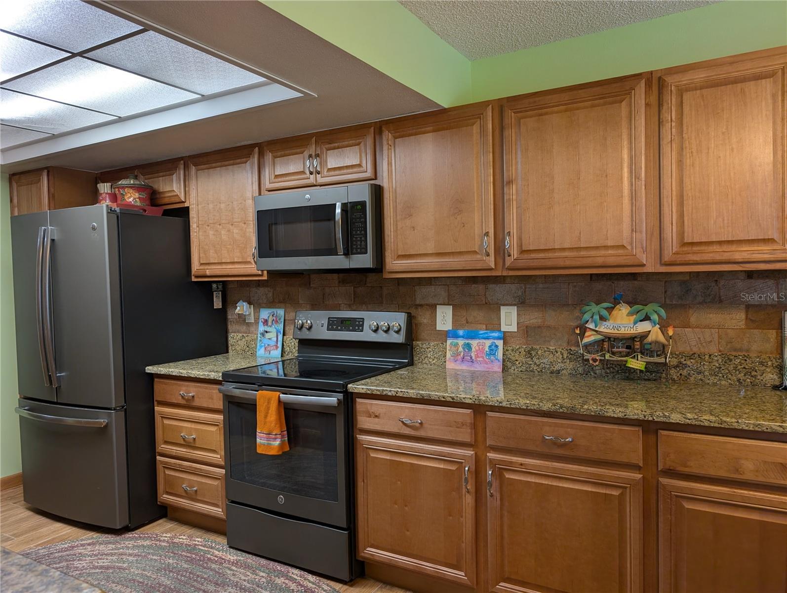Kitchen appliances include French door frig w/ice maker, glass top range and microwave hood.  Very neutral decor of Honey Oak cabinetry w/brushed nickel hardware, granite countertop and rustic tile backsplash.