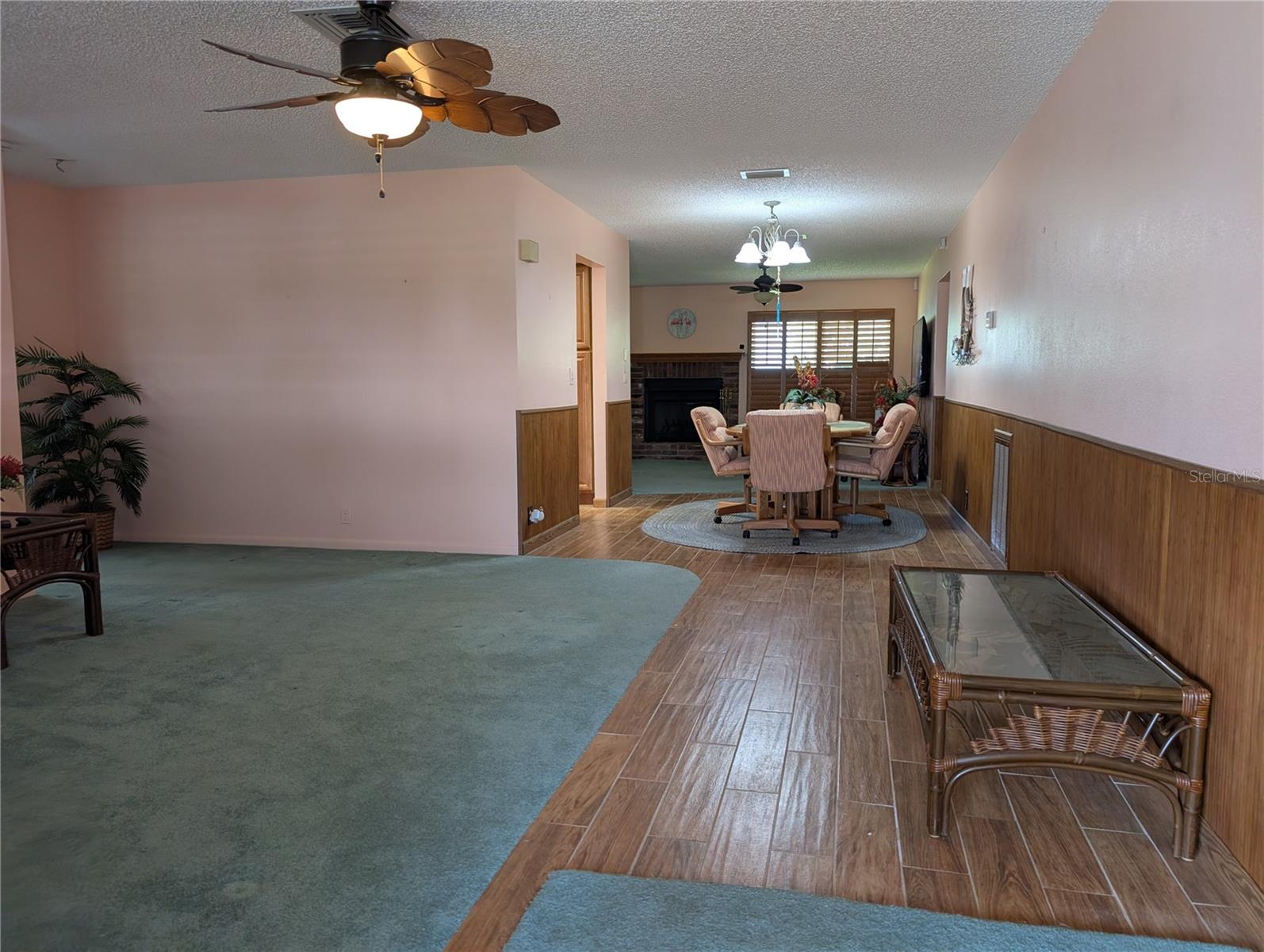 WELCOME IN...the rich warm interior decor features wood plank tile flooring, tropical ceiling fans, bamboo wainscoting and honey oak plantation shutters throughout. View from front entry thru living room, dining room to Florida room. Guest suite is to left of living room. Kitchen is left of dining room. Primary suite is right of Florida room.