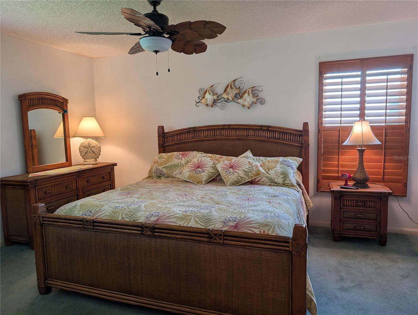 Spacious master bedroom features carpeting, tropical ceiling fan and the honey oak plantation shutters.