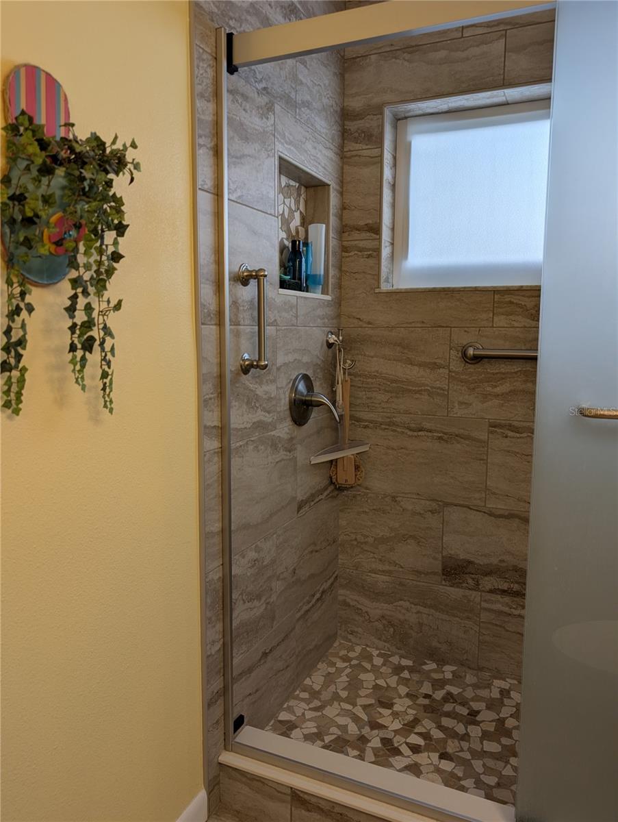 View of stunning tiled shower with brushed nickel hardware and grab bars. Window provides natural light and airflow.