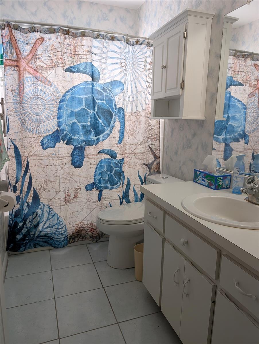 Main bath features white vanity, comfort height commode, tile flooring, medicine chest and a modified tub.